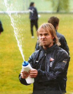 Bildet viser Dagfinn Enerly fra spillerkarrieren hvor han spruter med en vannflaske på treningsfeltet.